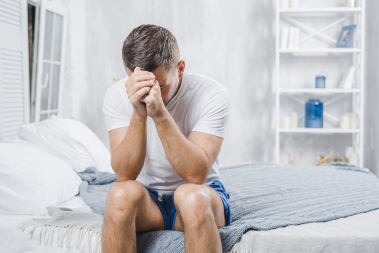 Homem sentado na cama frustrado