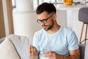 Homem com copo de água na mão e remédios