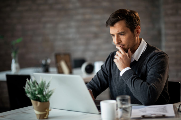 Homem sentado na frente do computador pensativo