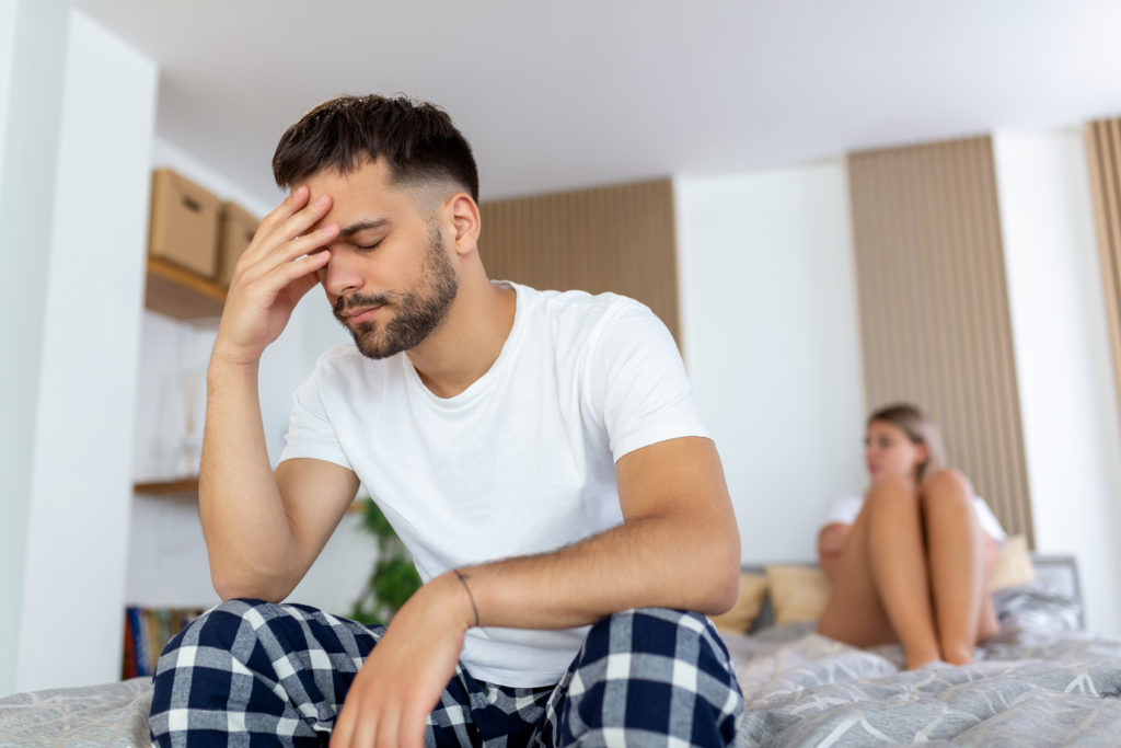 Homem sentado na cama com a mão na cabeça